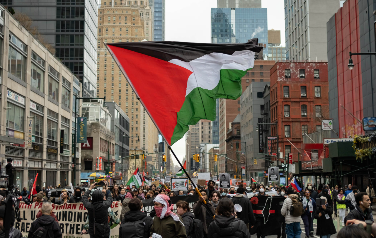 PRO-PALESTINIAN PROTESTERS IN TIMES SQUARE CHANTING AND HOLDING PALESTINIAN FLAGS AND SIGNS READING