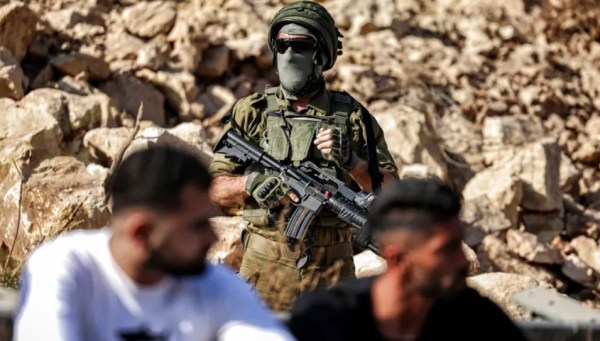 An Israeli soldier stands guard as Palestinians gather in protest at the site of a new road under construction for the use of Israeli settlers near the Palestinian village of Beit Ur al-Fauqa, west of Ramallah, in the occupied West Bank, on September 29, 2025